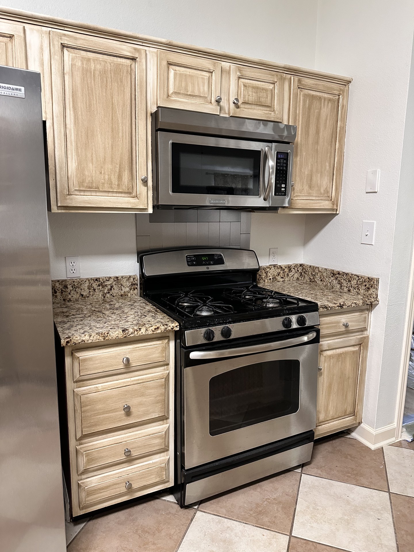 Worn beige cabinets around the stove and stainless appliances before painting in Austin