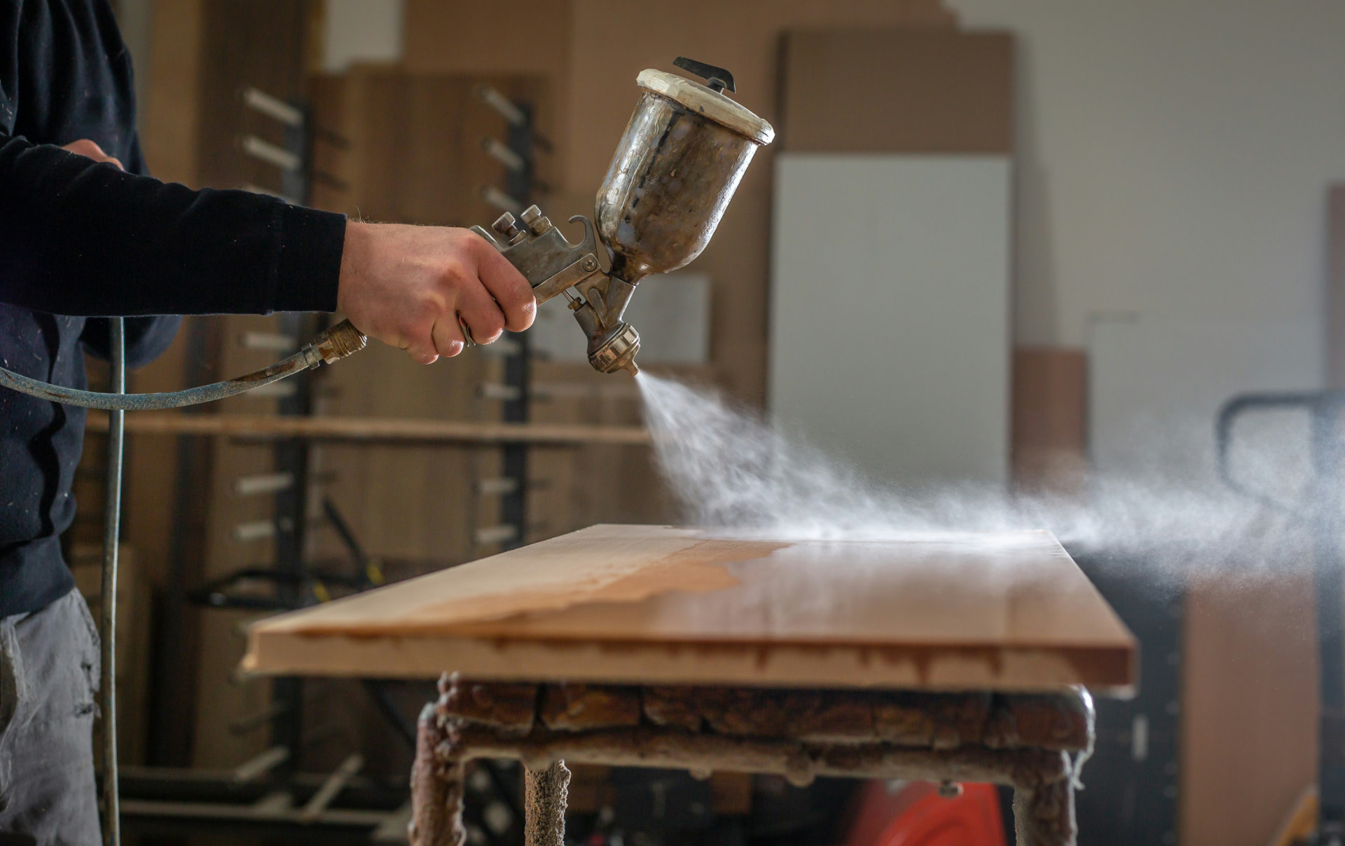 A finisher spraying finish onto a wood panel in the workshop