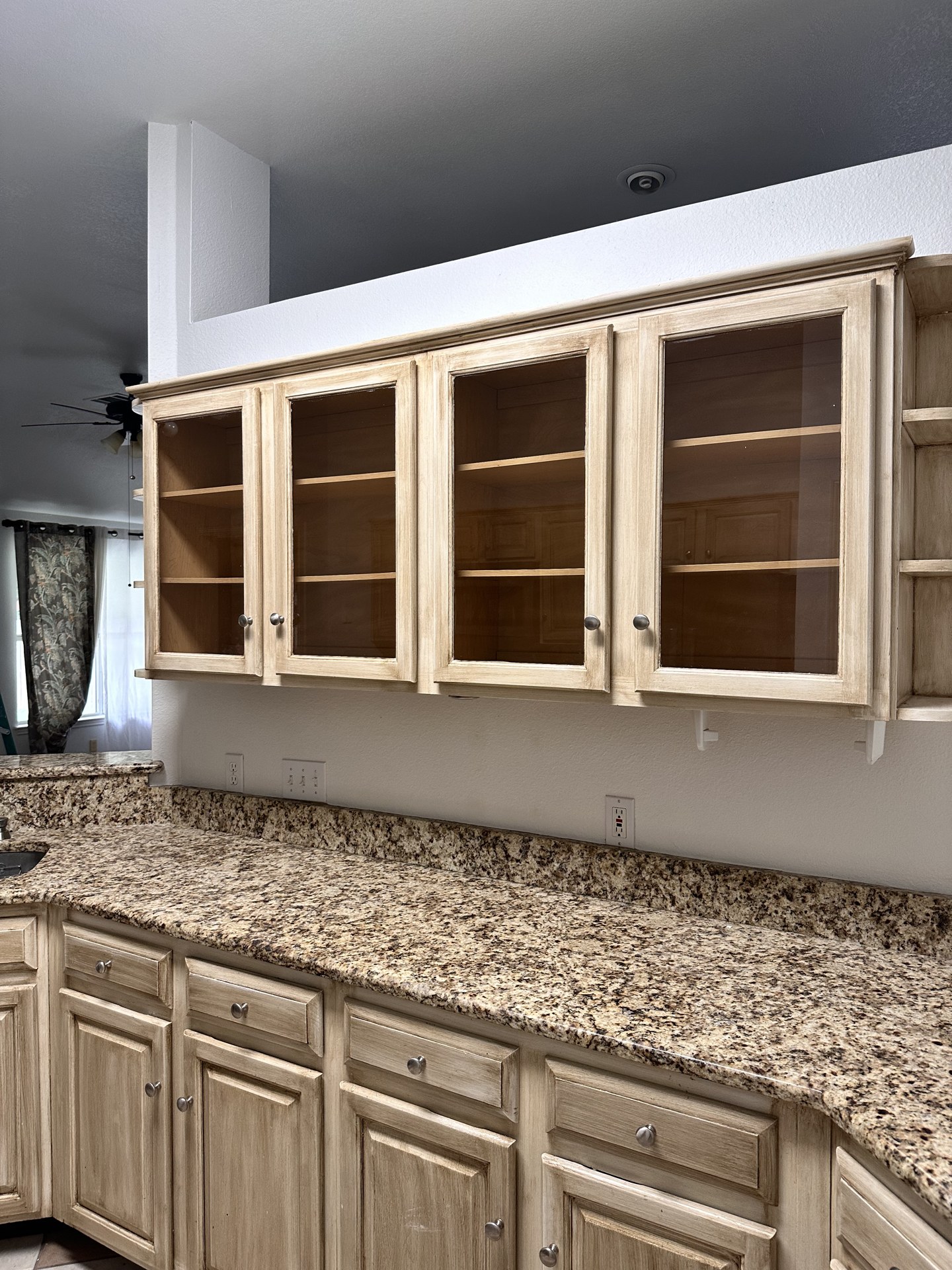 Glass-front upper cabinets and worn beige lower cabinets before painting in Austin